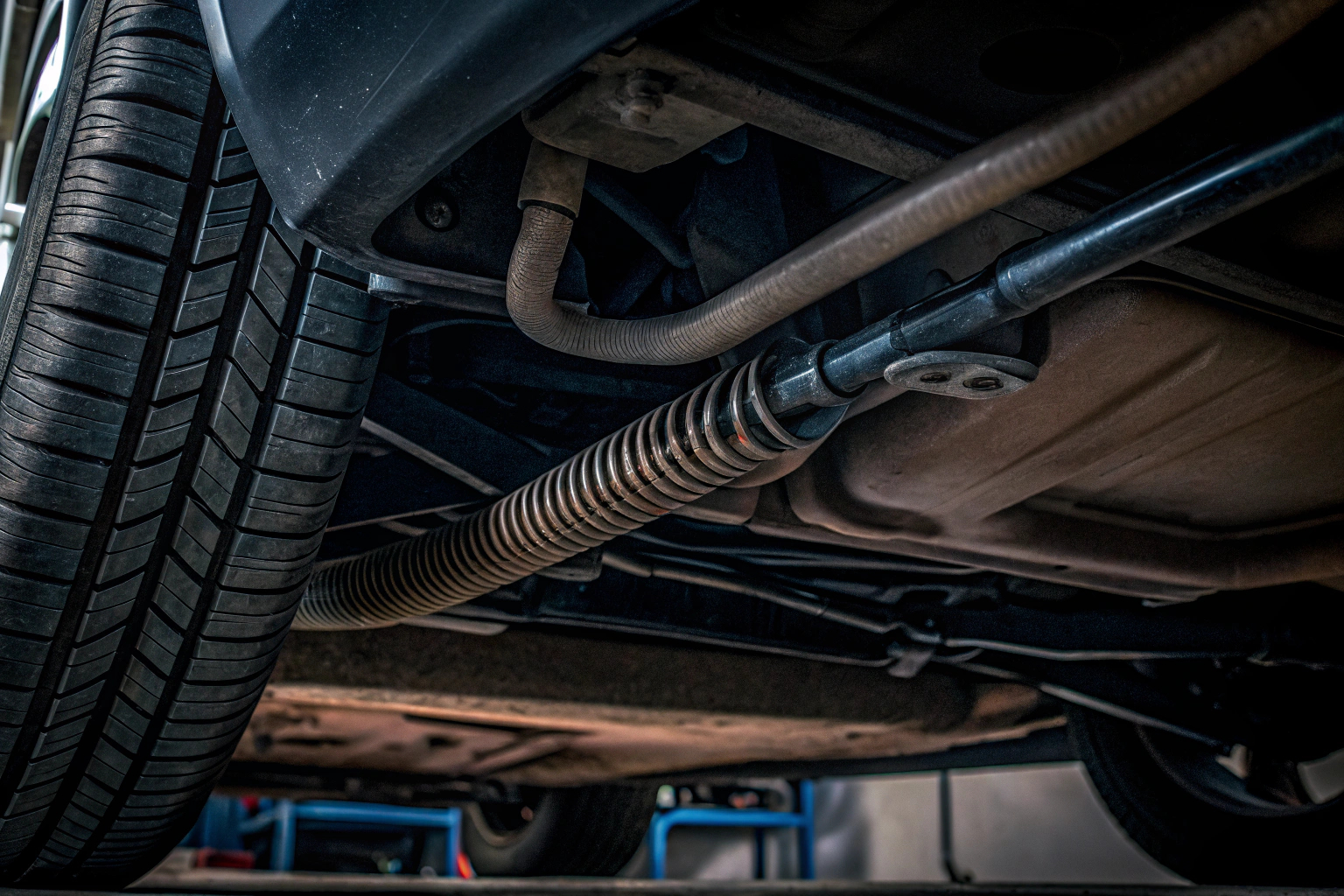 Detailaufnahme eines Autos von unten, das auf einem Hebebühne steht. Der Fokus liegt auf den Schläuchen und Federungen des Fahrzeugs. Unterboden eines Fahrzeugs mit Fokus auf Schläuche und Federn