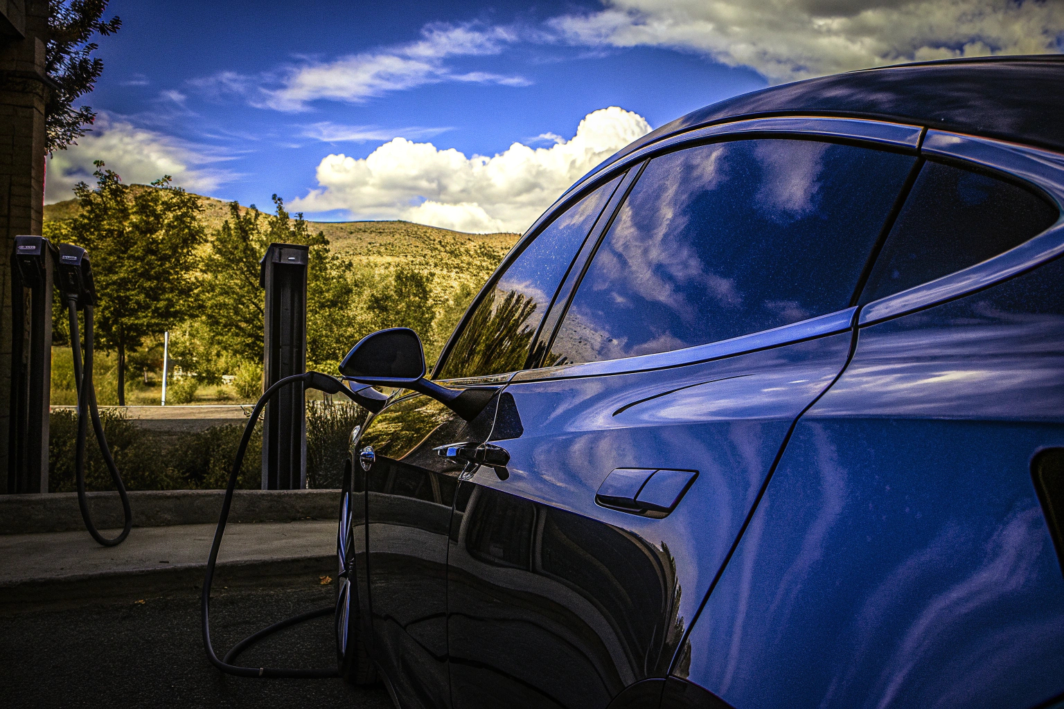 Ein Elektroauto an einer Ladestation mit grüner Landschaft im Hintergrund. Elektroauto an Ladestation
