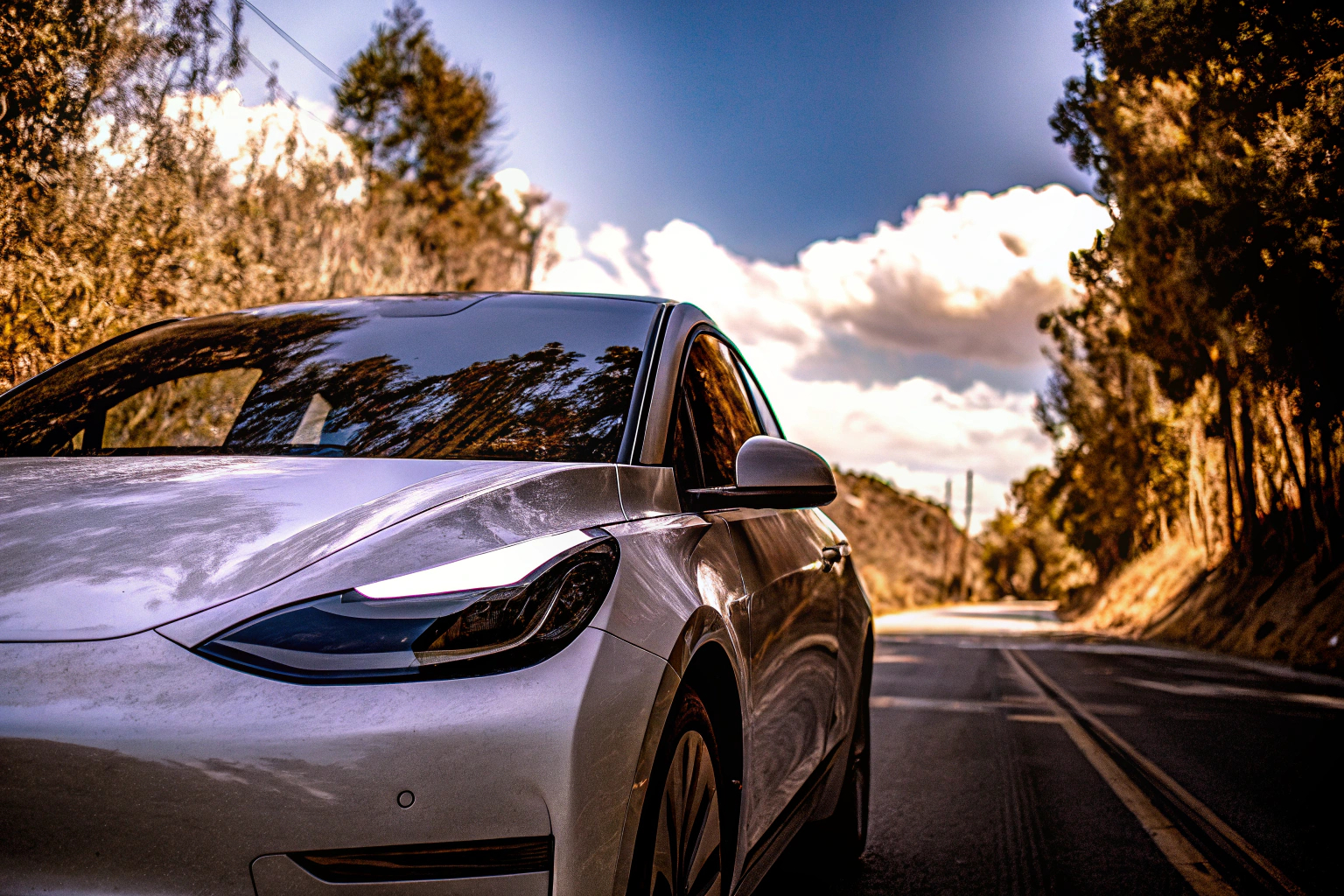 Ein Elektroauto auf einer Straße, umgeben von Bäumen, mit einem sonnigen Himmel im Hintergrund Elektroauto auf Straße