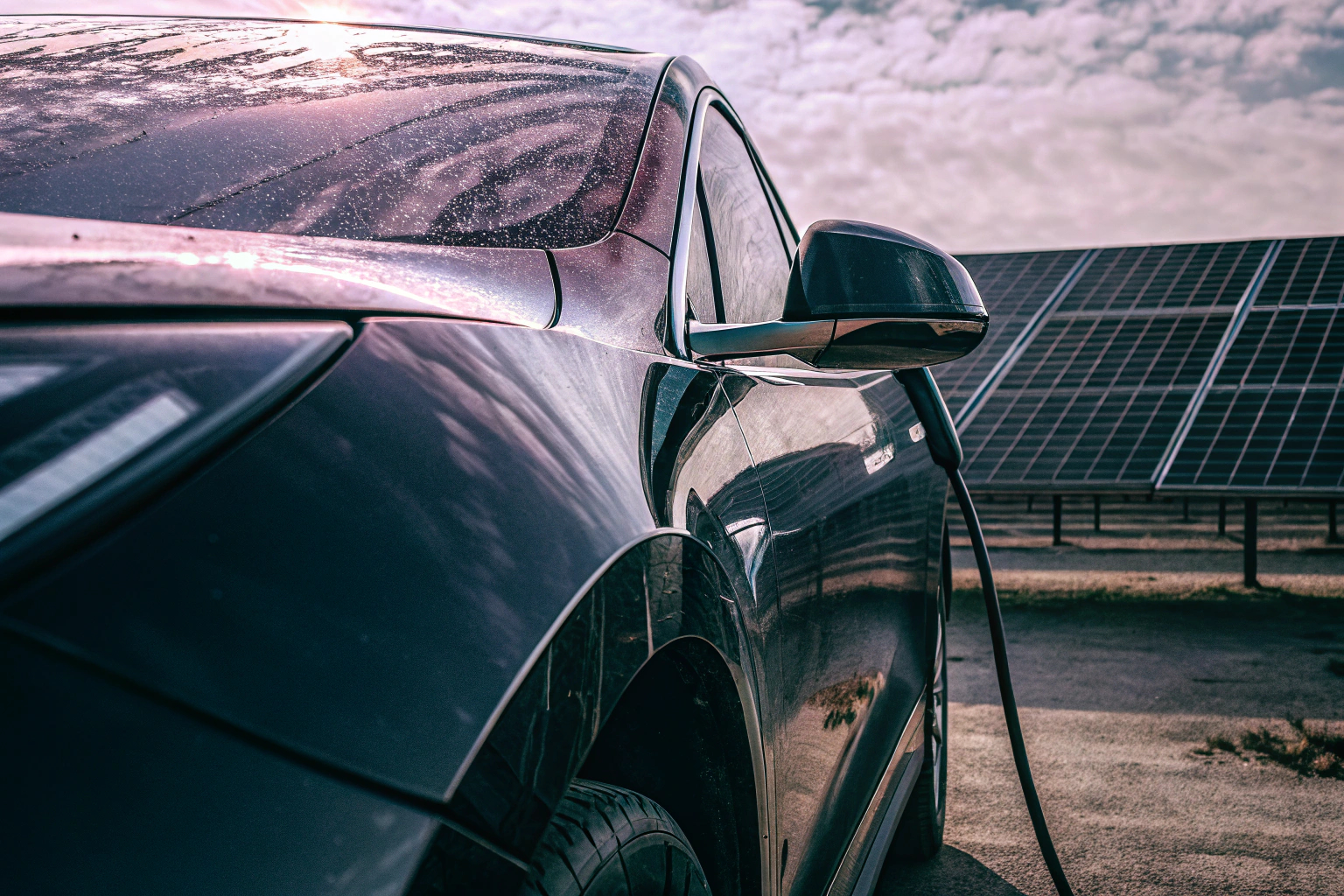 Ein Elektroauto, das an einer Ladestation aufgeladen wird. Im Hintergrund sind Solarzellen zu sehen, die erneuerbare Energie liefern. Elektroauto an Ladestation