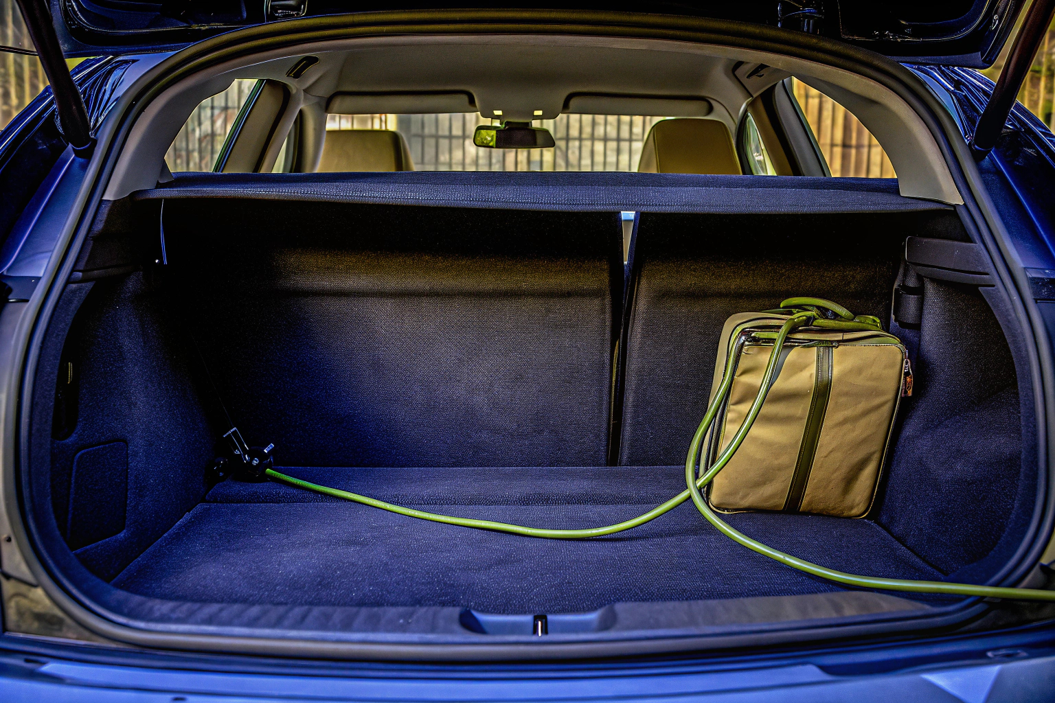 Ein Fahrer verstaut ein Ladekabel in einer speziell dafür vorgesehenen Tasche im Kofferraum seines Elektroautos. Ladekabeltasche im Kofferraum