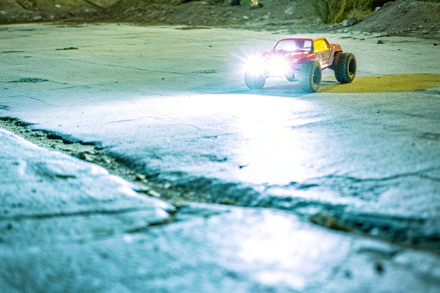 Ein ferngesteuertes Auto, das bei Nacht mit eingeschalteten Scheinwerfern fährt, hebt sich durch die Beleuchtung von der dunklen Umgebung ab. RC-Auto bei Nacht