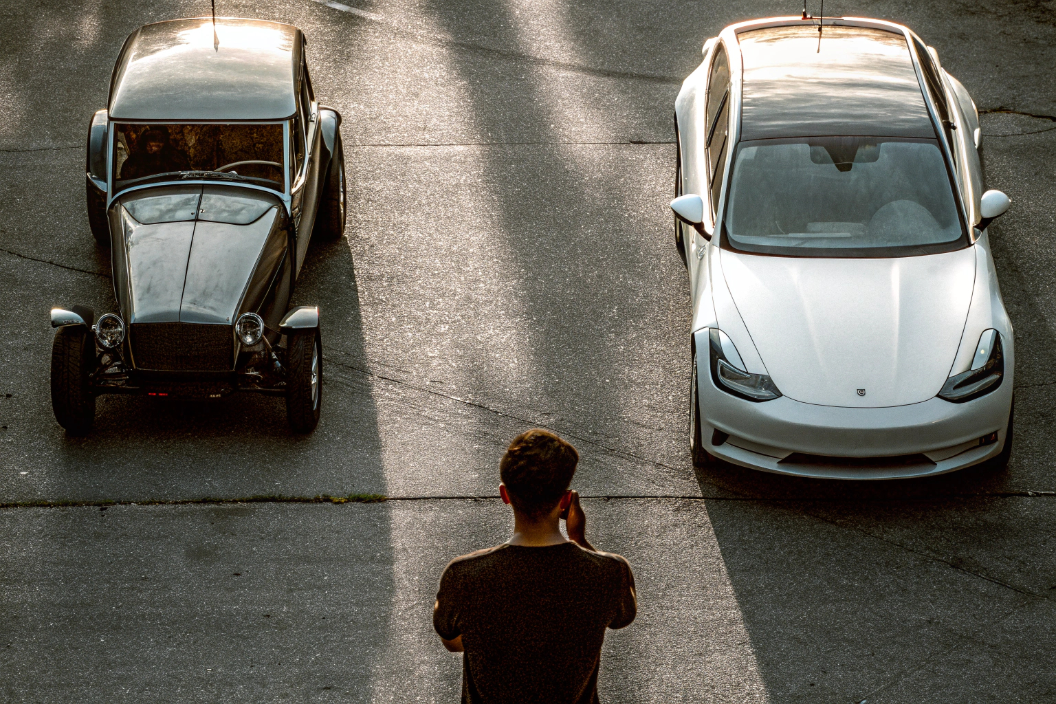 Ein Mann steht nachdenklich zwischen einem Elektroauto und einem Verbrenner, unschlüssig, welches er wählen soll. Entscheidung zwischen Elektroauto und Verbrenner