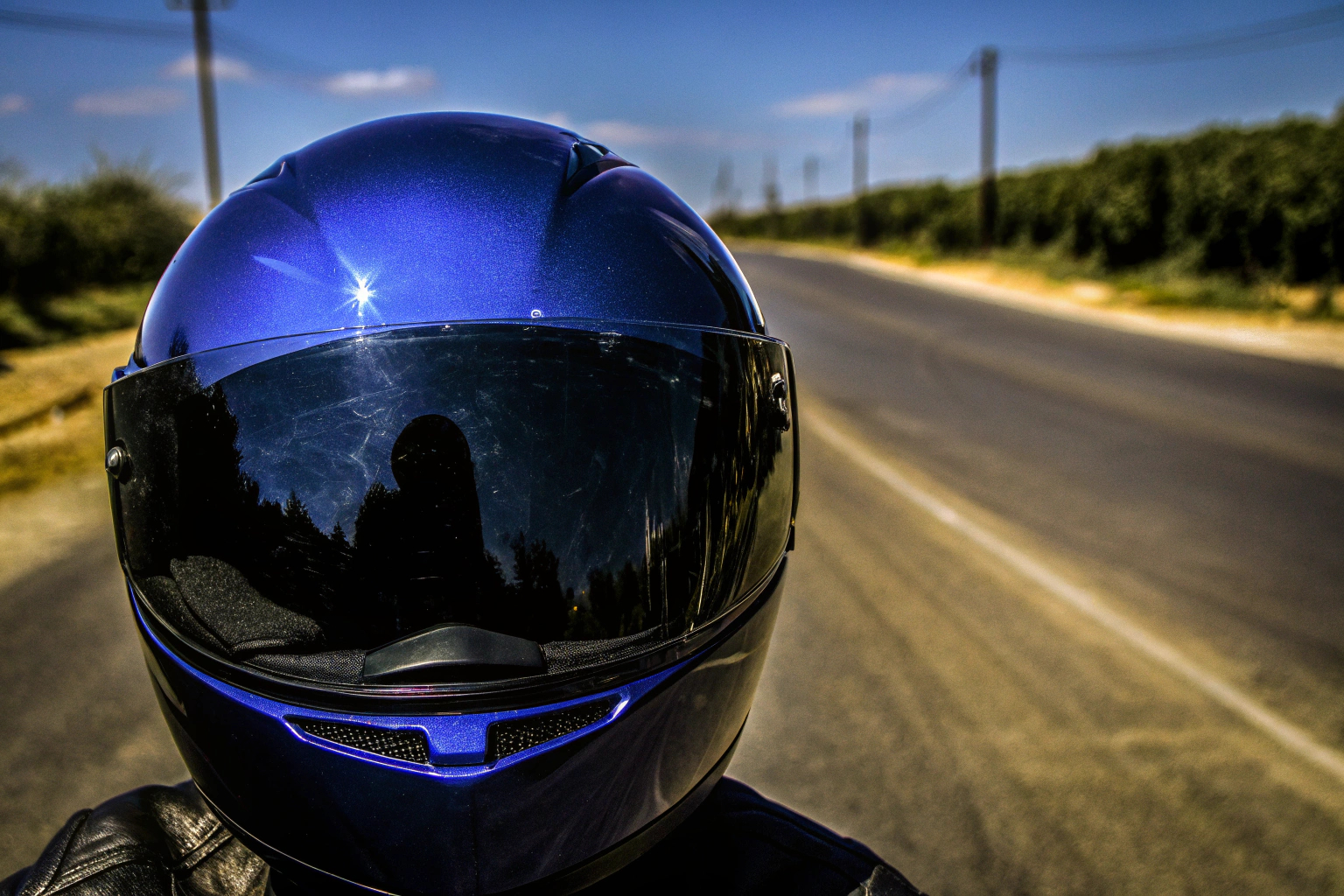 Ein Motorradfahrer, der einen Helm mit heruntergeklapptem Sonnenvisier trägt, während er auf einer sonnigen Straße fährt. Motorradfahrer mit Sonnenvisierhelm