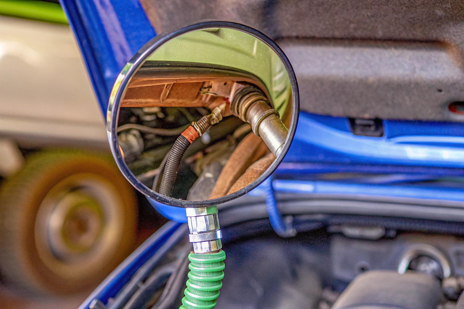 Eine Person verwendet einen 360° drehbaren Inspektionsspiegel, um unter die Motorhaube eines Autos zu schauen. Inspektionsspiegel verwendet unter Motorhaube